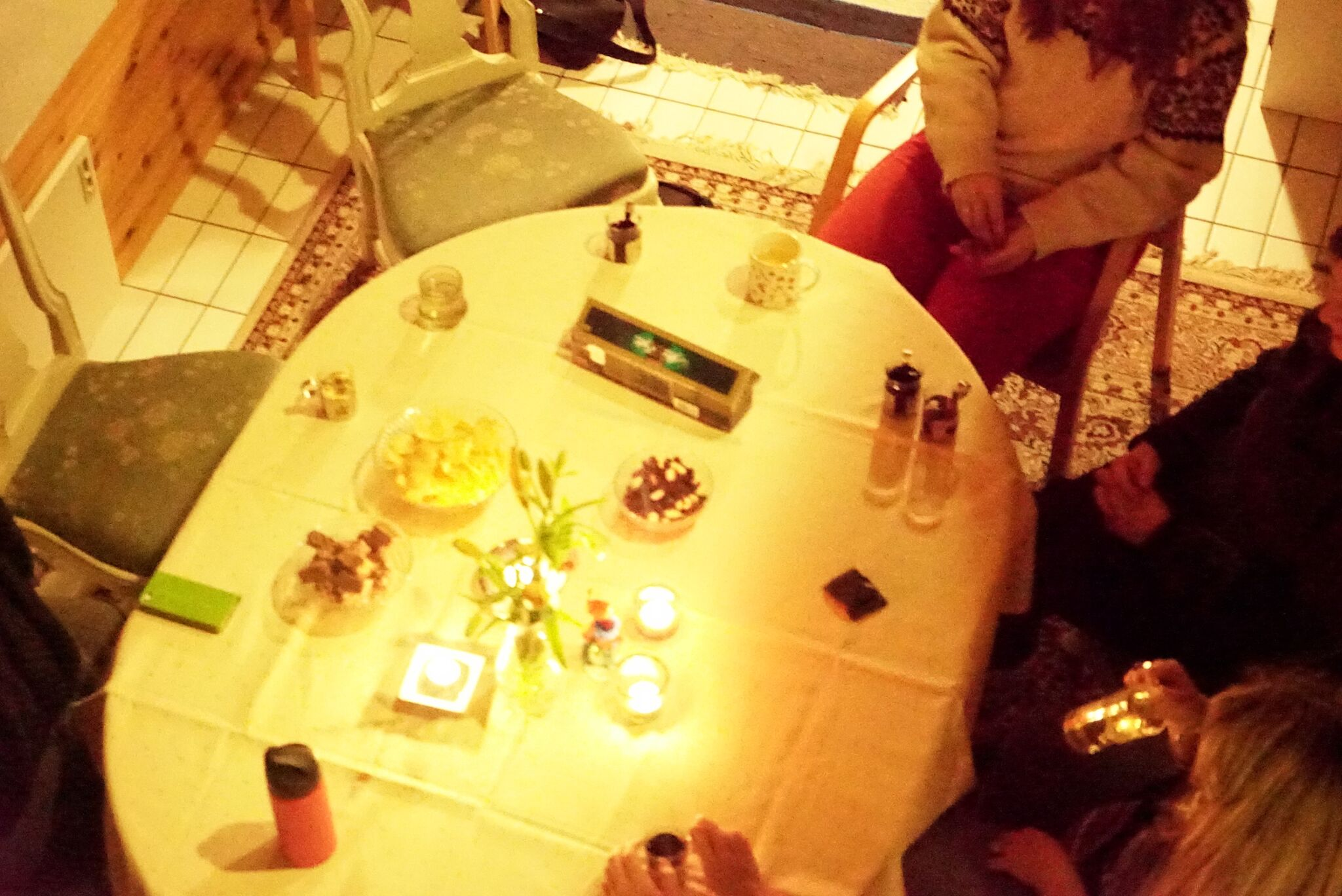 A dining table pictured from above with candles and three people sitting around