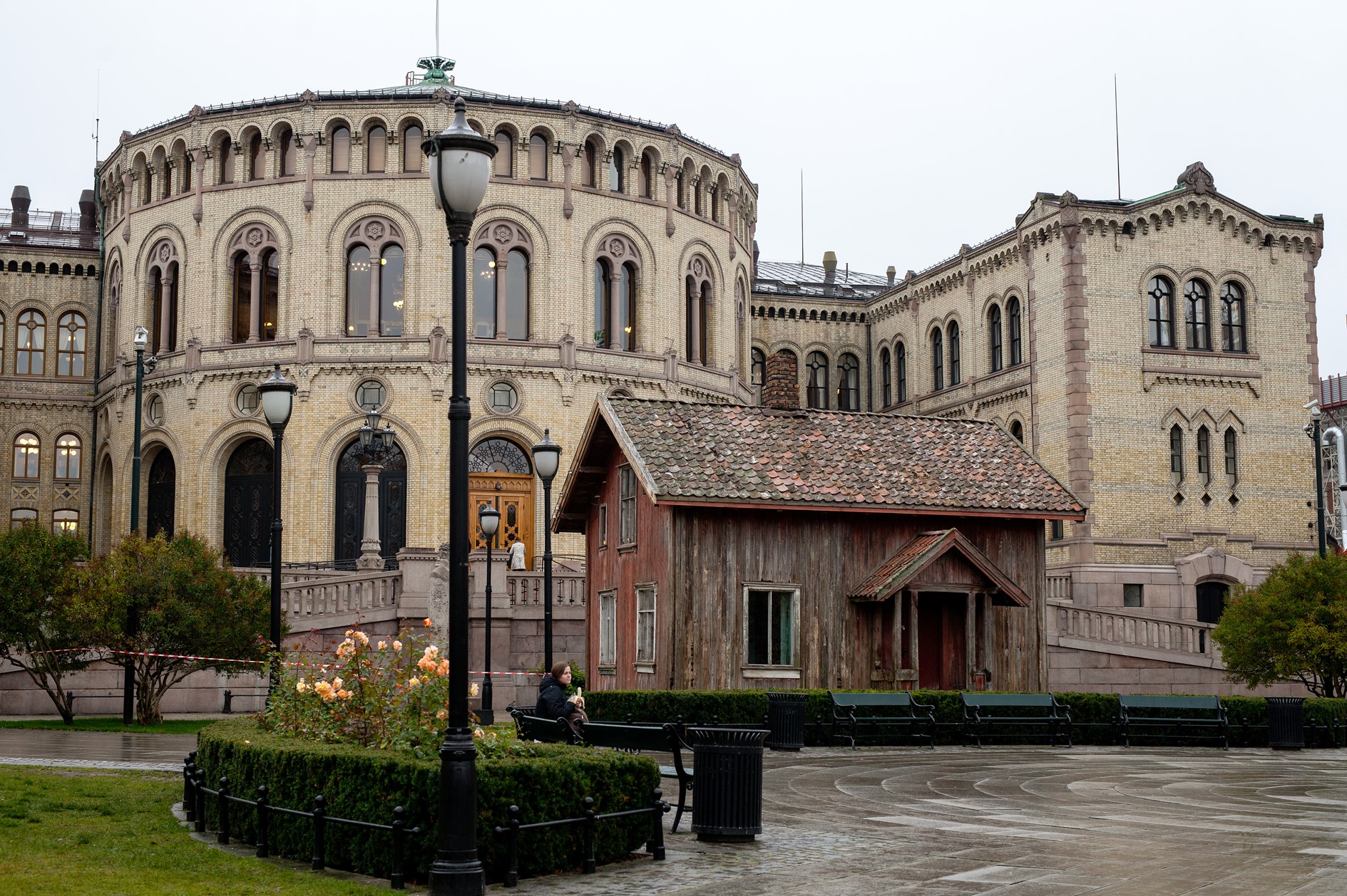 Foto av Stortinget og Eidsvolls plass med et gammelt, slitt hus foran.