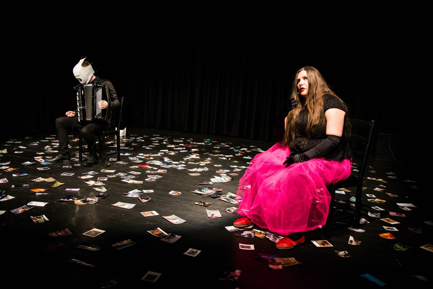 Photo from performance by Dahlsveen. Seated actor and seated accordeonist. Many photos lying on the floor. Photo by BGBØRSUM and Fortellerfestivalen.