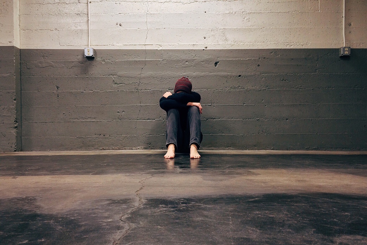A person sitting against a wall hiding their face