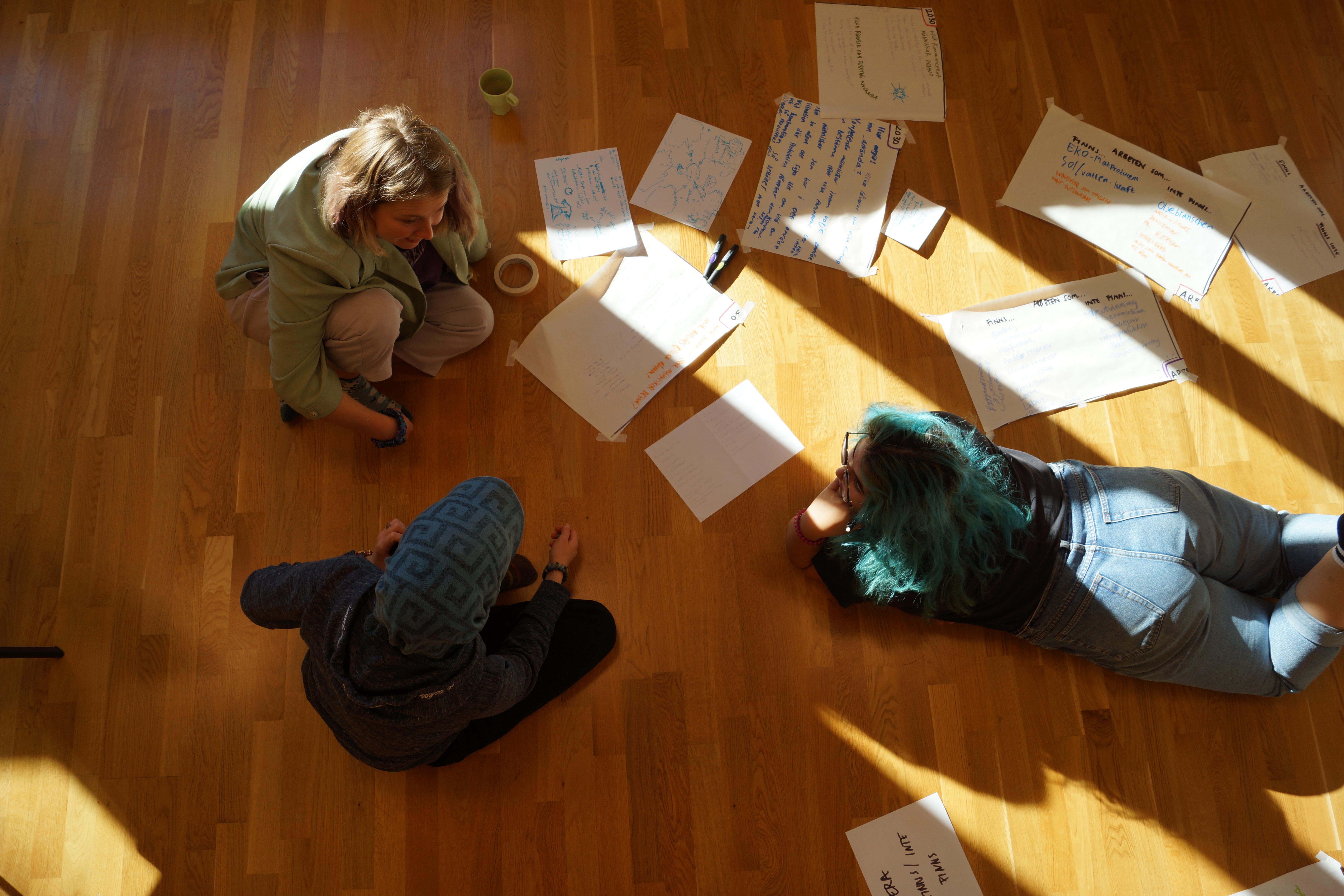 Three people on the floor with papers with writing spread all over.\