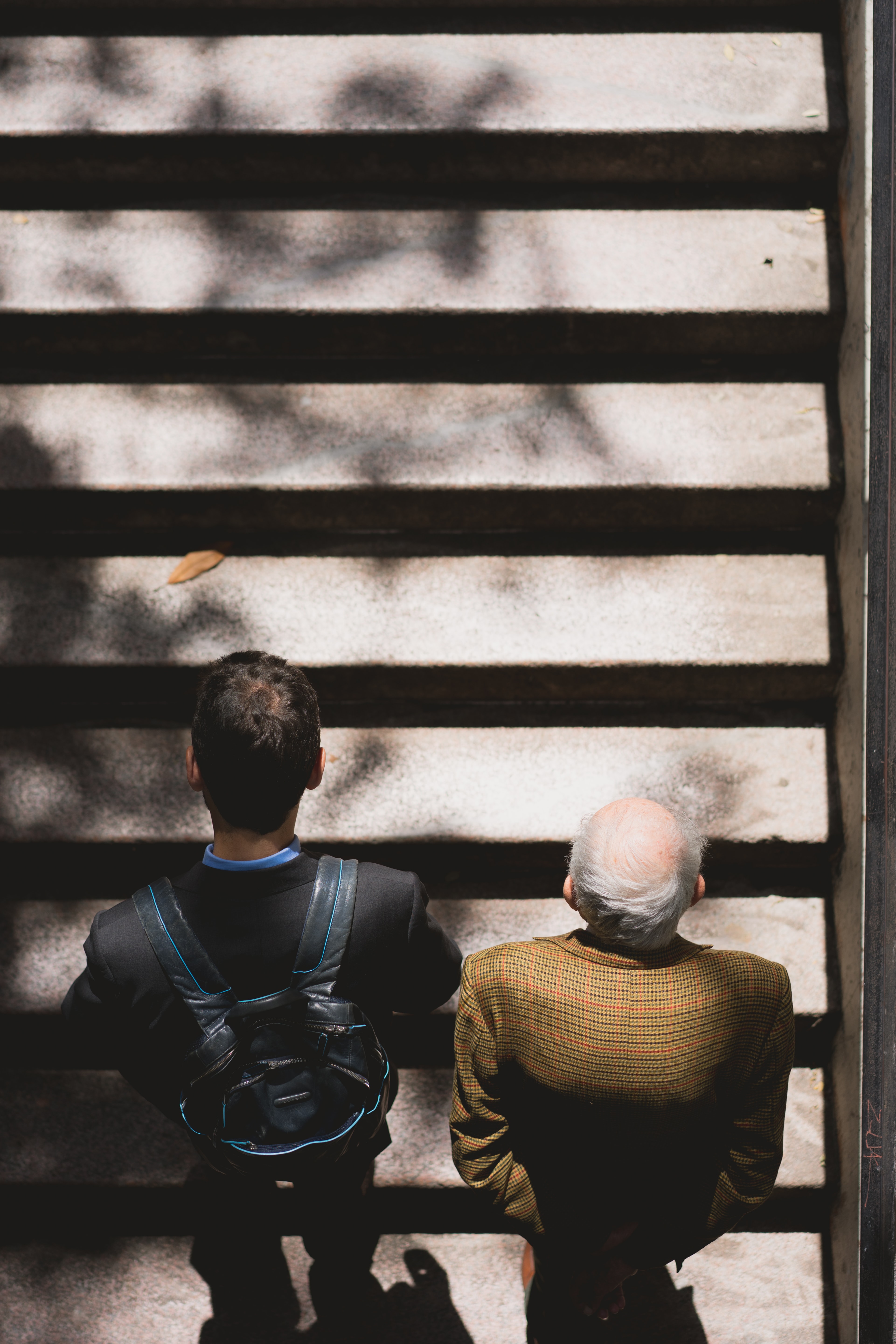 A young and an old man viewed from above, walking away from the camera climbing stairs. Picture by John Moeses Bauan on Unsplash