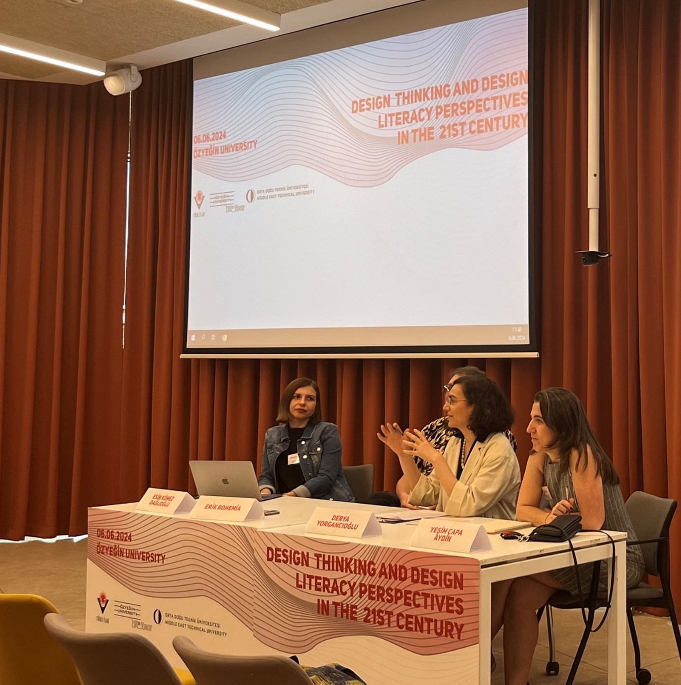 Four people behind a long table in front of a screen showing the conference logo