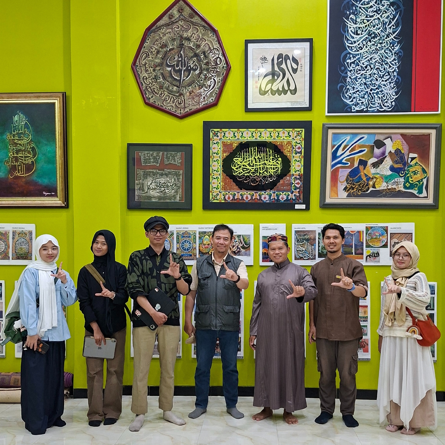 The image shows seven people, three women and four men, standing in front of a wall of Islamic paintings on display. They were conducting field data collection as part of a study on Islamic painting.